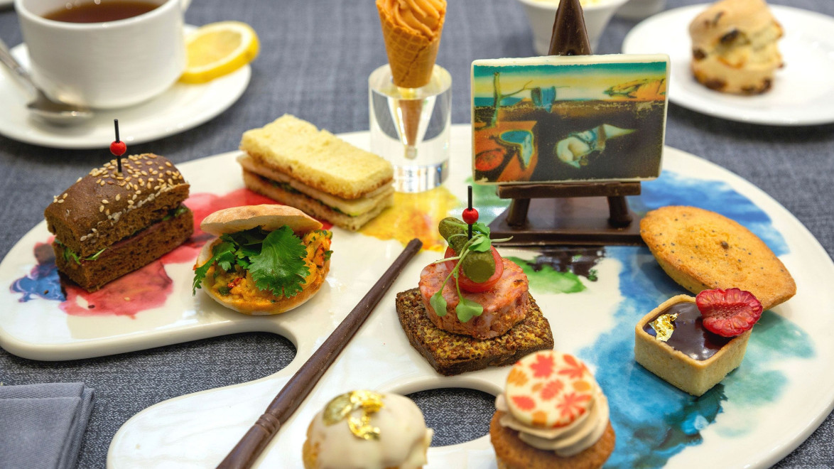 Platter of assorted gourmet appetizers and desserts served on an artist palette with a painting easel decor.