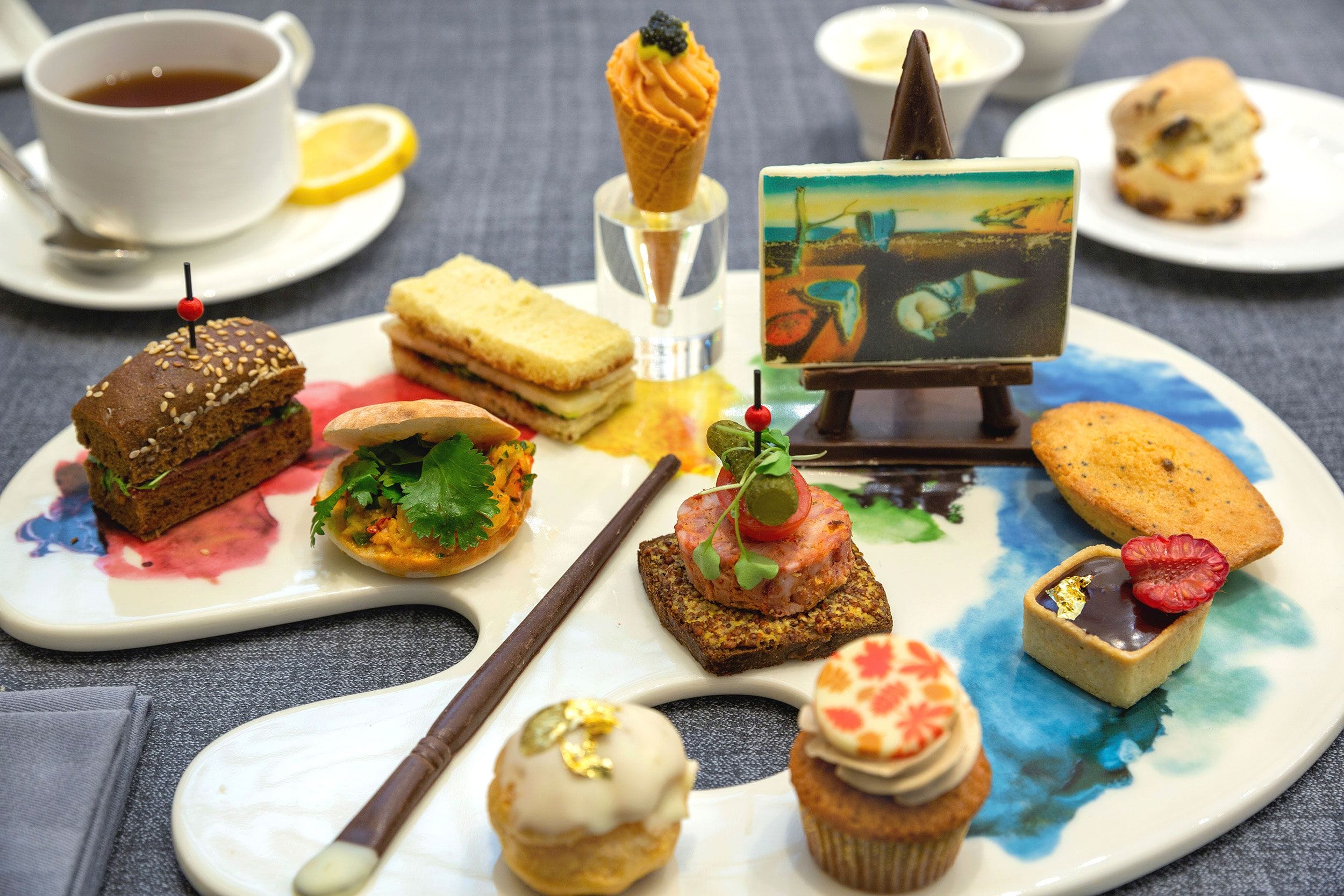 Platter of assorted gourmet appetizers and desserts served on an artist palette with a painting easel decor.