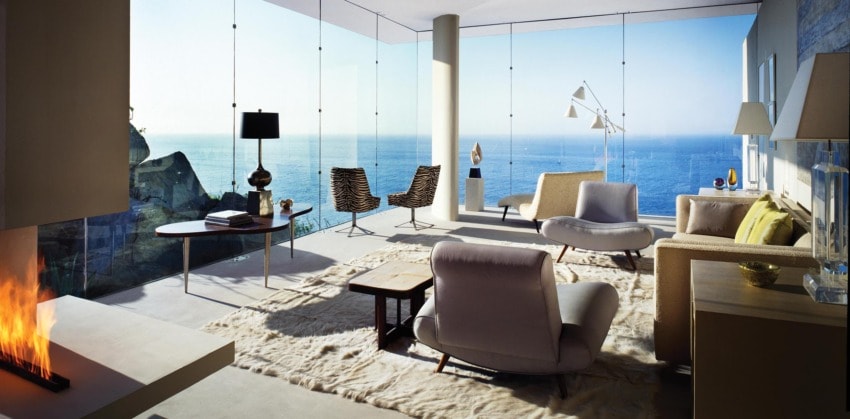Modern living room with large windows, ocean view, cozy furniture, and warm fireplace.