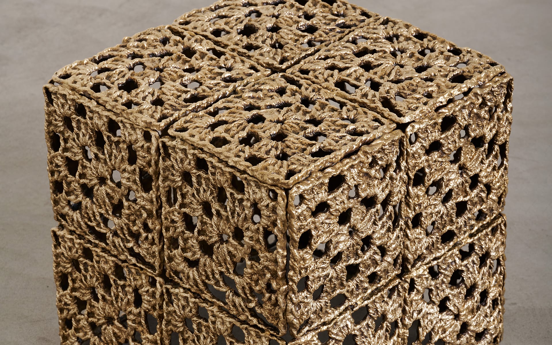 Intricately designed woven cube sculpture made of natural fibers on a gray background.