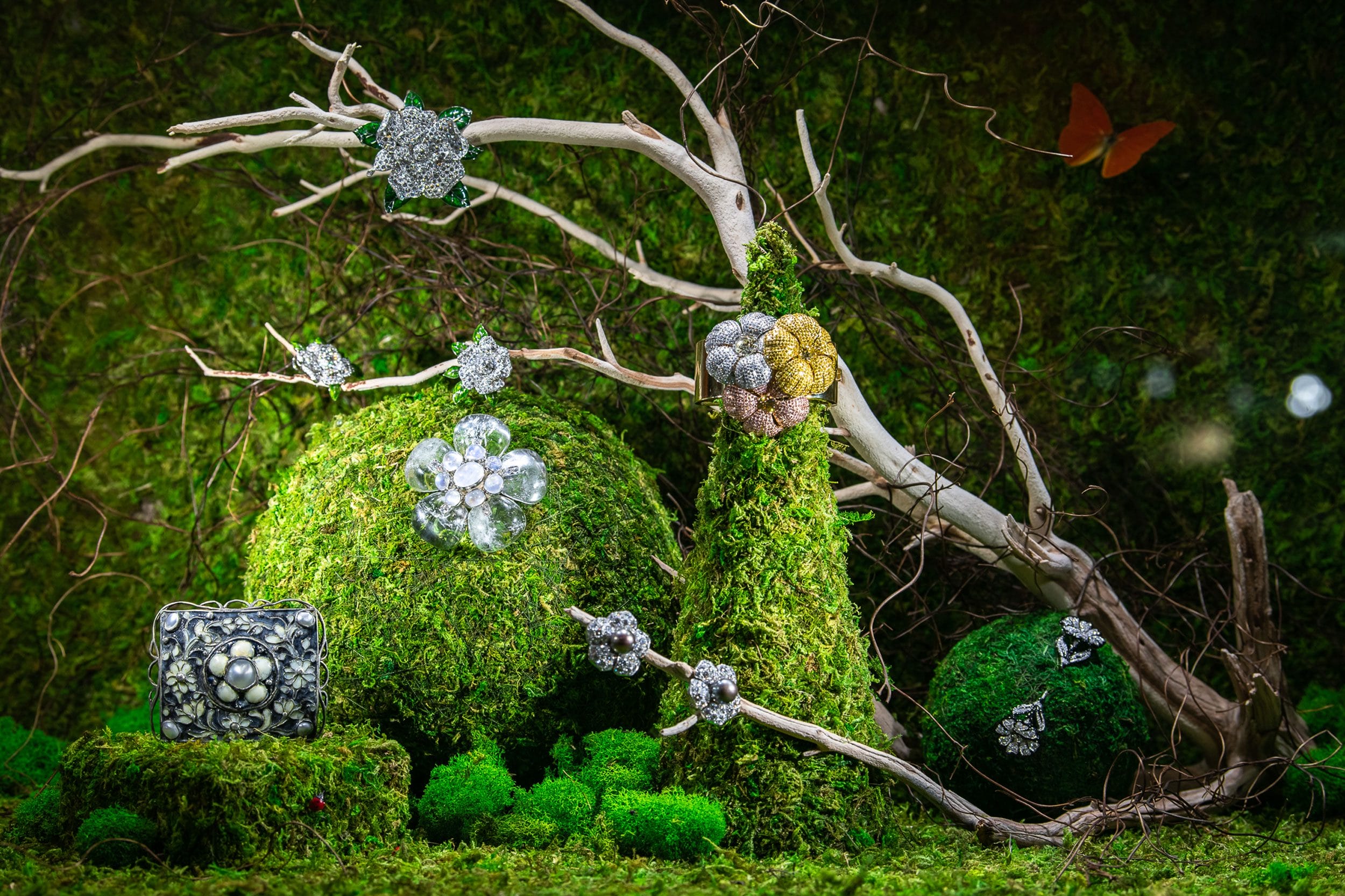 Jewelry displayed on moss-covered branches with a butterfly and dark green background.