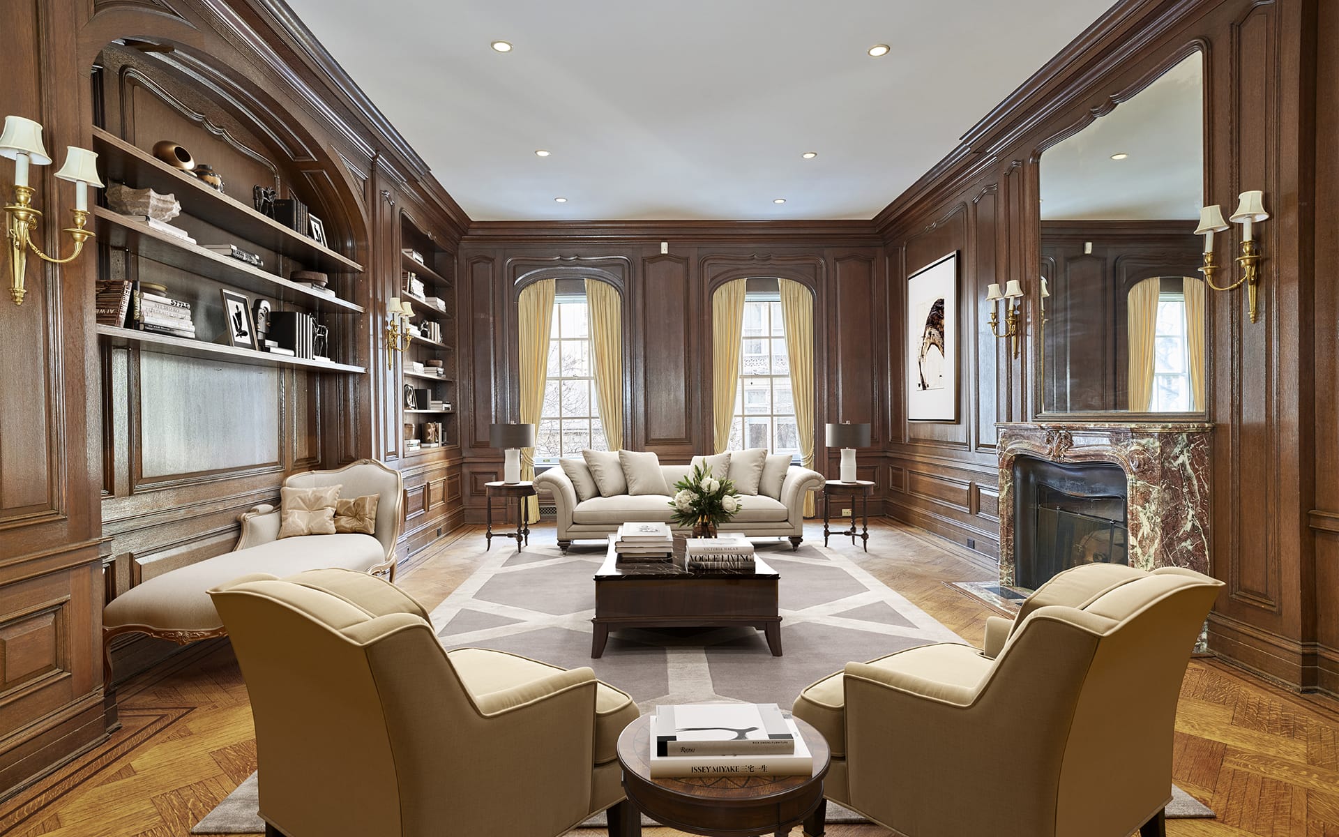Elegant living room with wooden paneling, large windows, and comfortable seating arranged around a central coffee table.