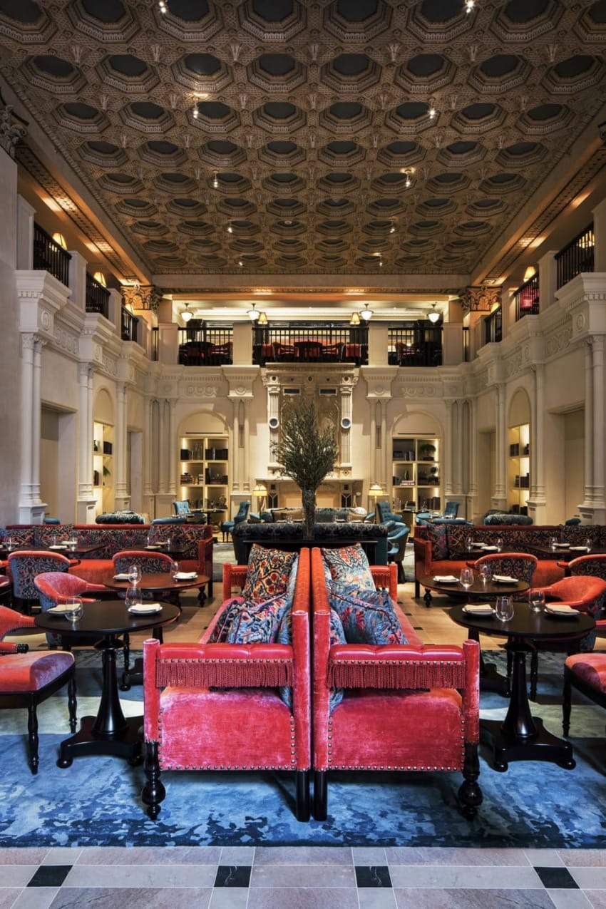 Luxurious hotel lounge with ornate ceiling, red sofas, and elegant lighting creating a sophisticated and inviting atmosphere.
