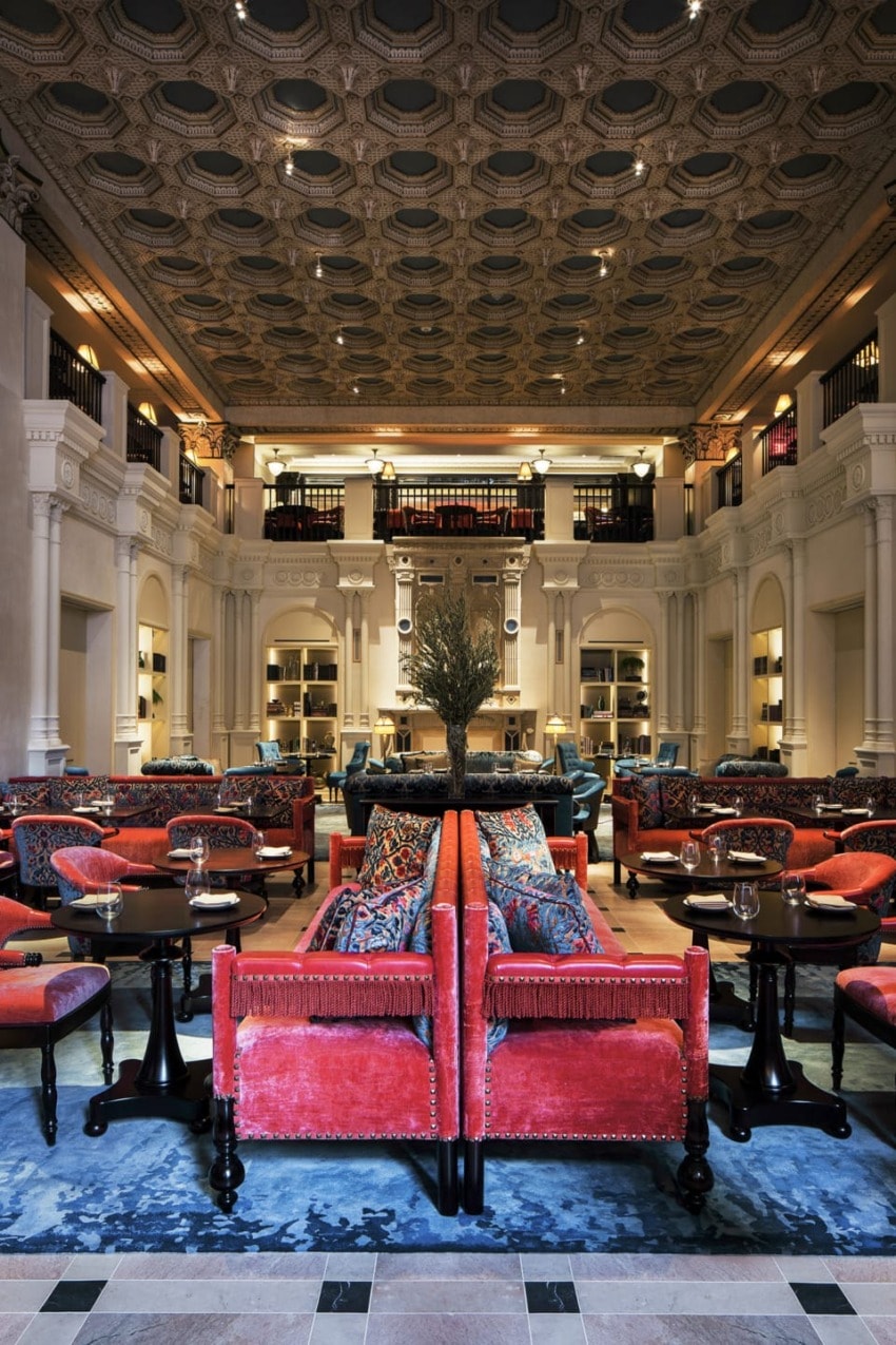 Luxurious hotel lounge with ornate ceiling, red sofas, and elegant lighting creating a sophisticated and inviting atmosphere.
