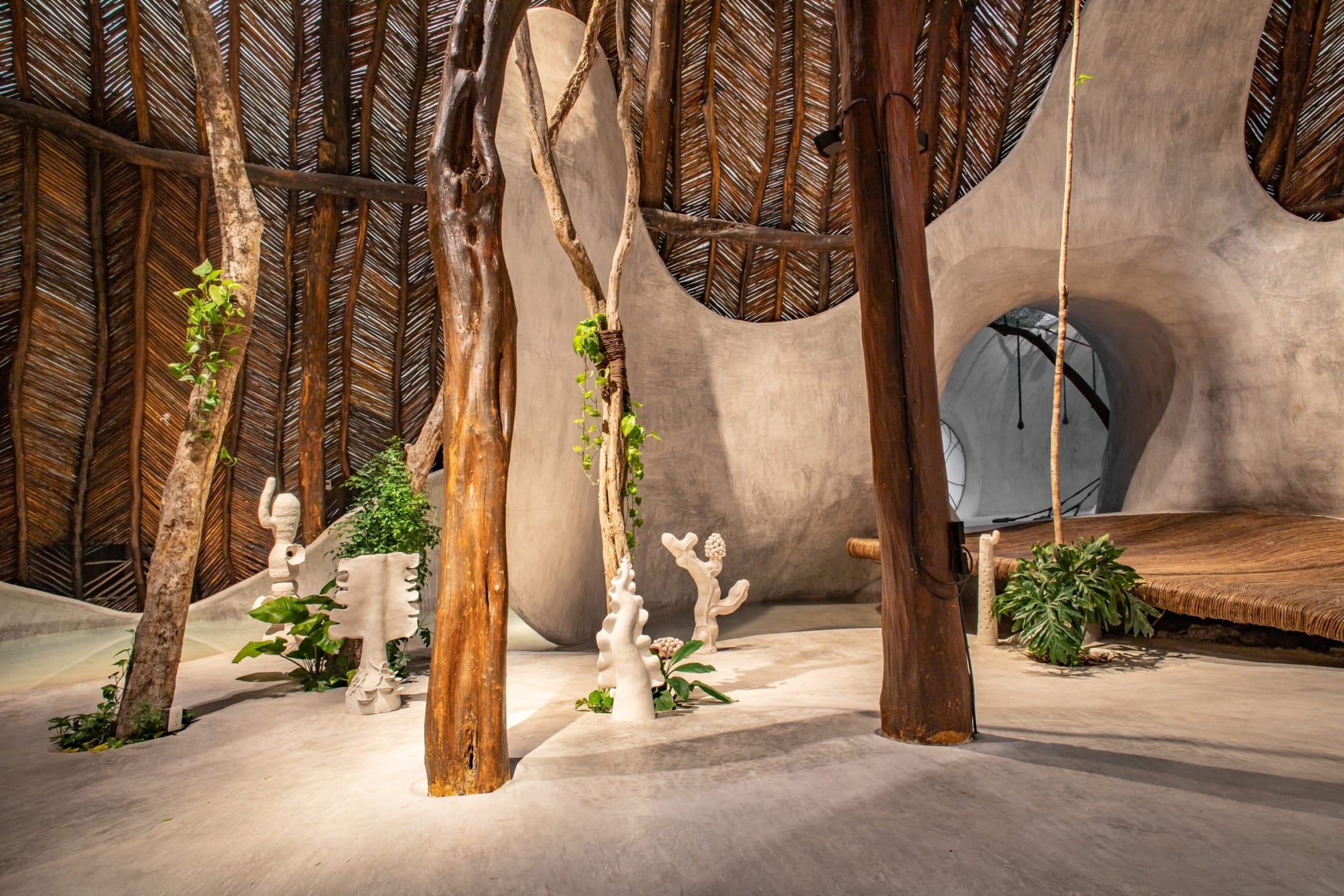 Interior of a unique eco-friendly space with wooden beams, plants, and artistic sculptures under a woven ceiling.