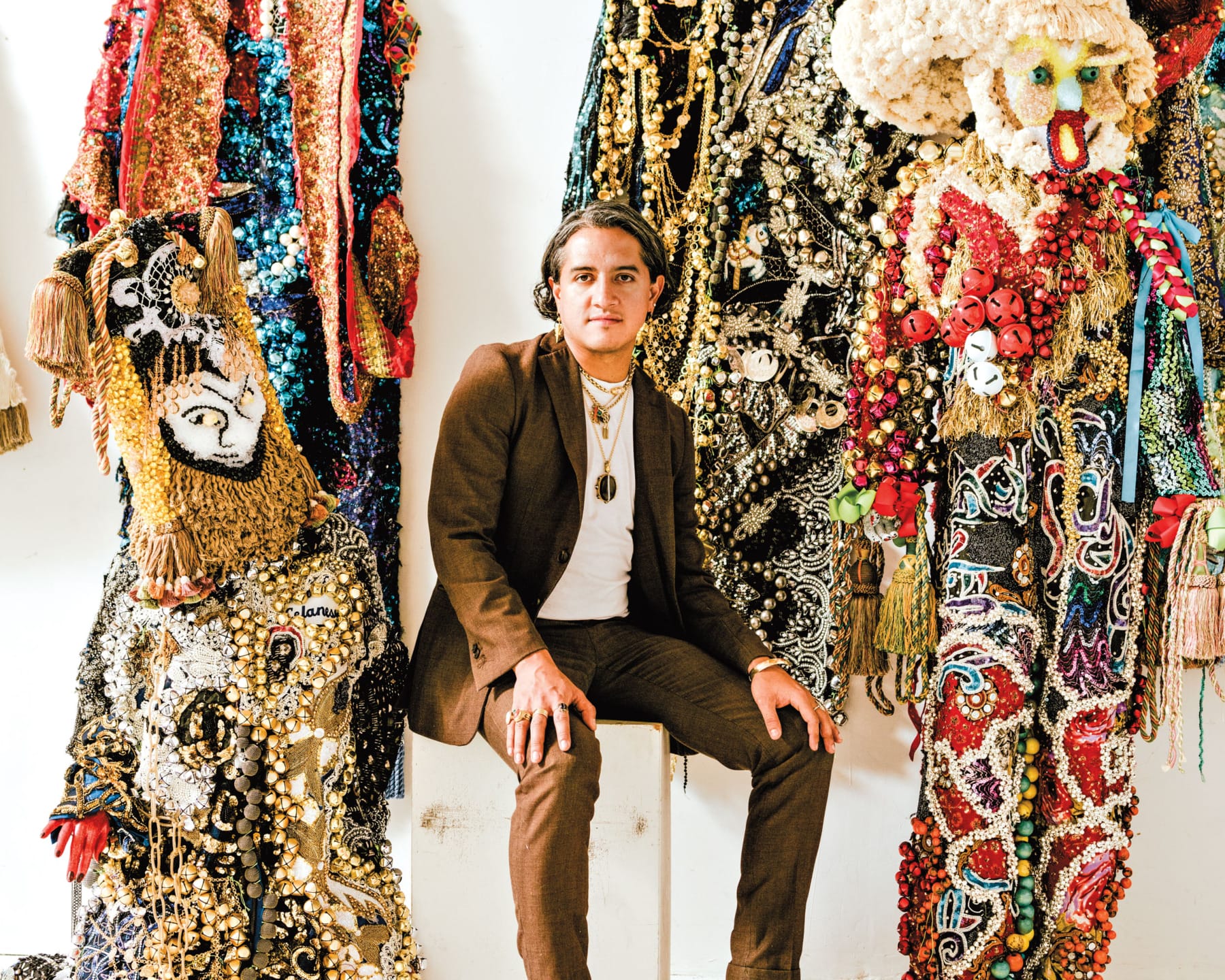 Person sitting amidst elaborate, colorful costumes adorned with sequins, beads, and intricate details.