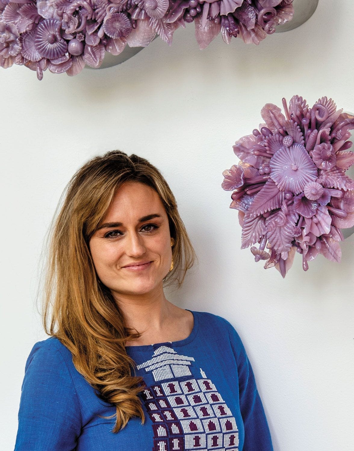 Woman in blue dress stands beside purple floral wall sculptures