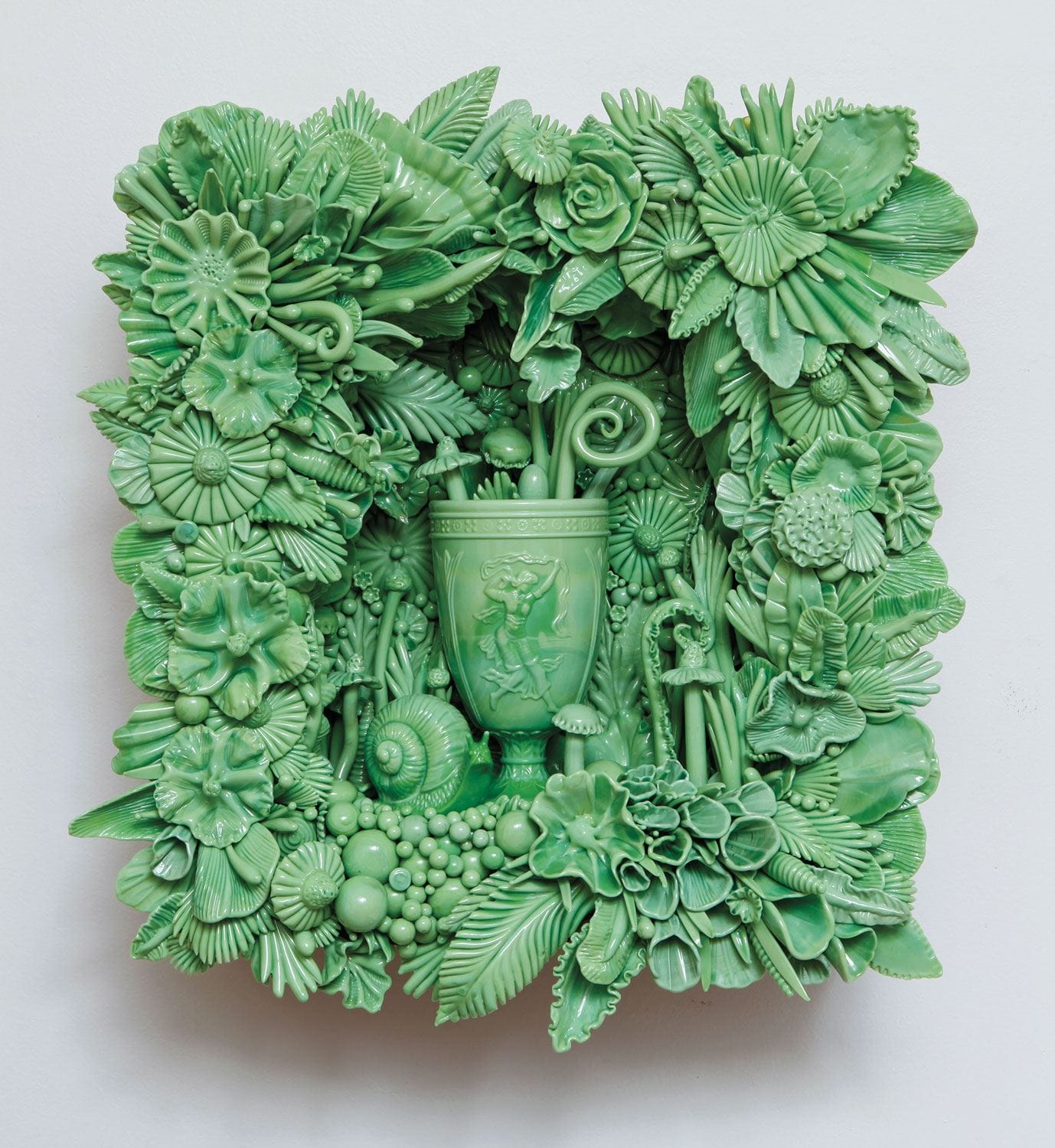 Green ceramic art piece with intricate floral patterns and central vase featuring detailed plant and leaf motifs.