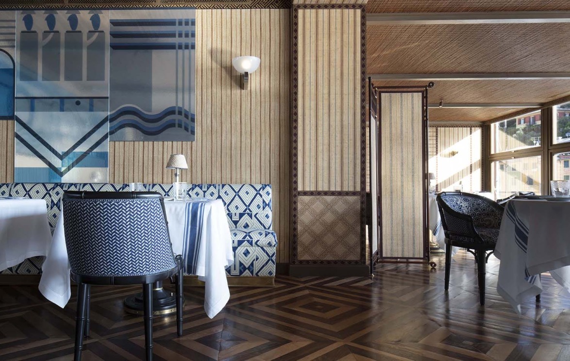Elegant restaurant interior with patterned walls, blue and white chairs, and wooden flooring.