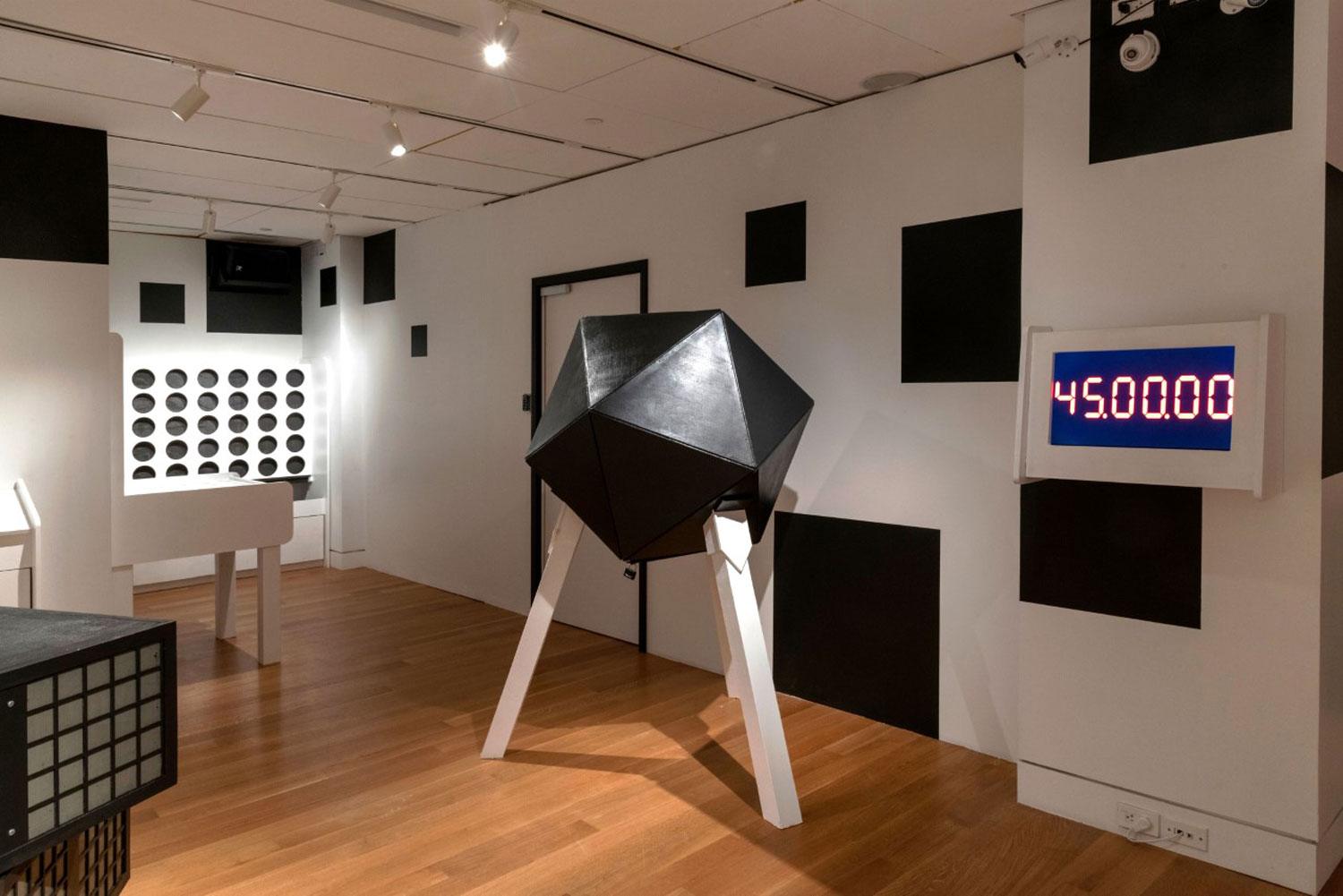 Modern art gallery with geometric sculptures and a digital timer displaying 45:00:00, wooden floor and white walls.