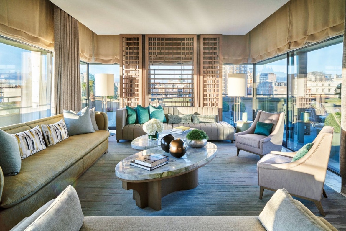 Luxurious living room with large windows, stylish sofas, patterned cushions, and a modern coffee table with decorative items.