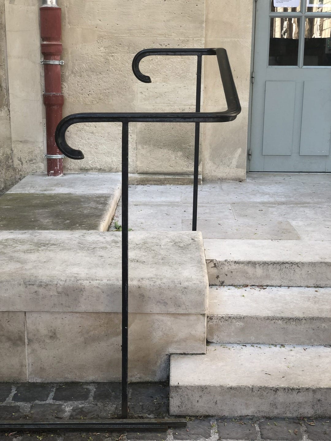 Unique black handrail artfully designed with elegant curves, standing beside stone steps and a closed door in the background.