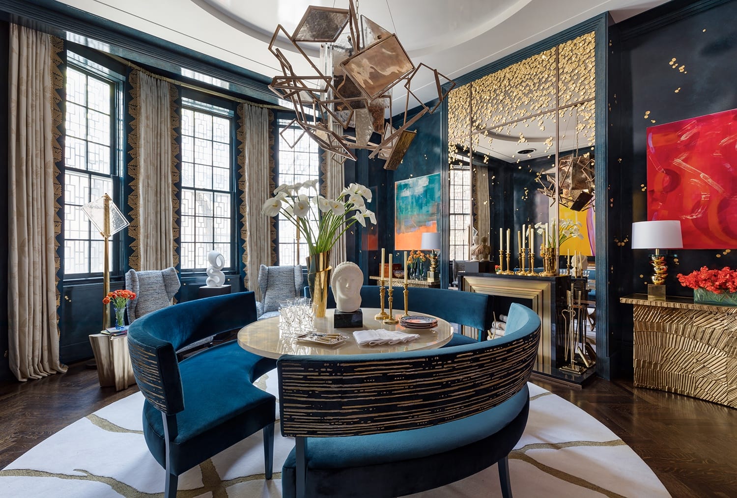 Luxurious dining room with modern decor, featuring a round table, blue seating, abstract art, and a geometric chandelier.