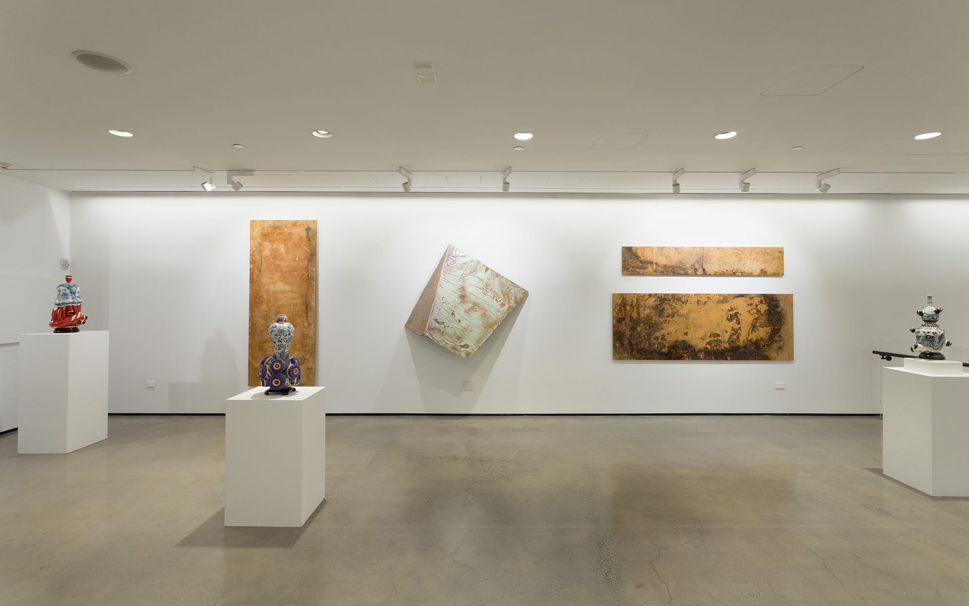 Contemporary art gallery with abstract paintings and intricate sculptures on white pedestals.