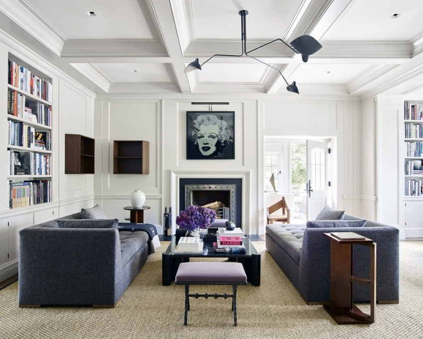 Modern living room with gray sofas, a black and white art piece above the fireplace, and bookshelves on each side