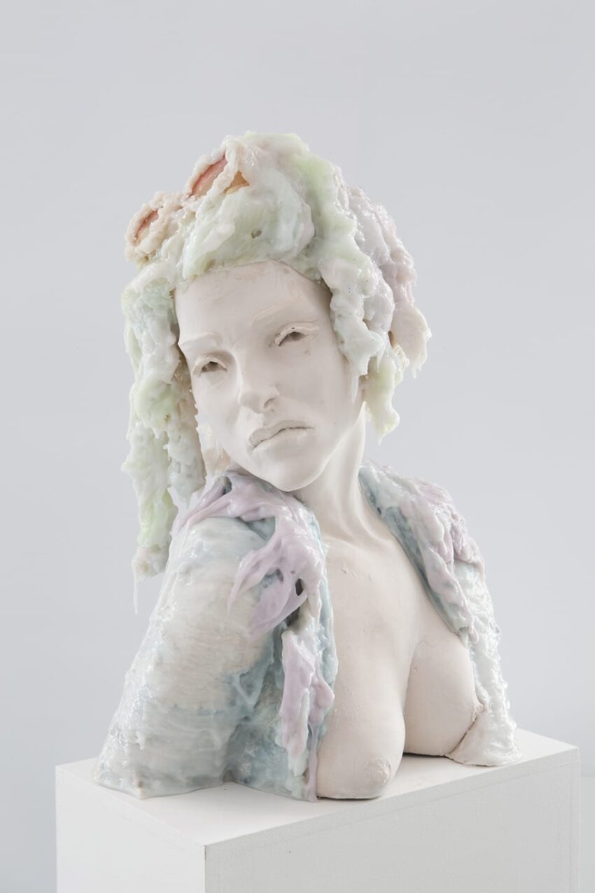 Ceramic sculpture of a woman with a detailed expression, draped in pastel-colored textures, displayed on a white pedestal.