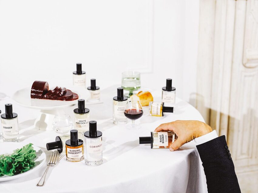 A table set with various perfume bottles, a glass of wine, and slices of bread and meat.