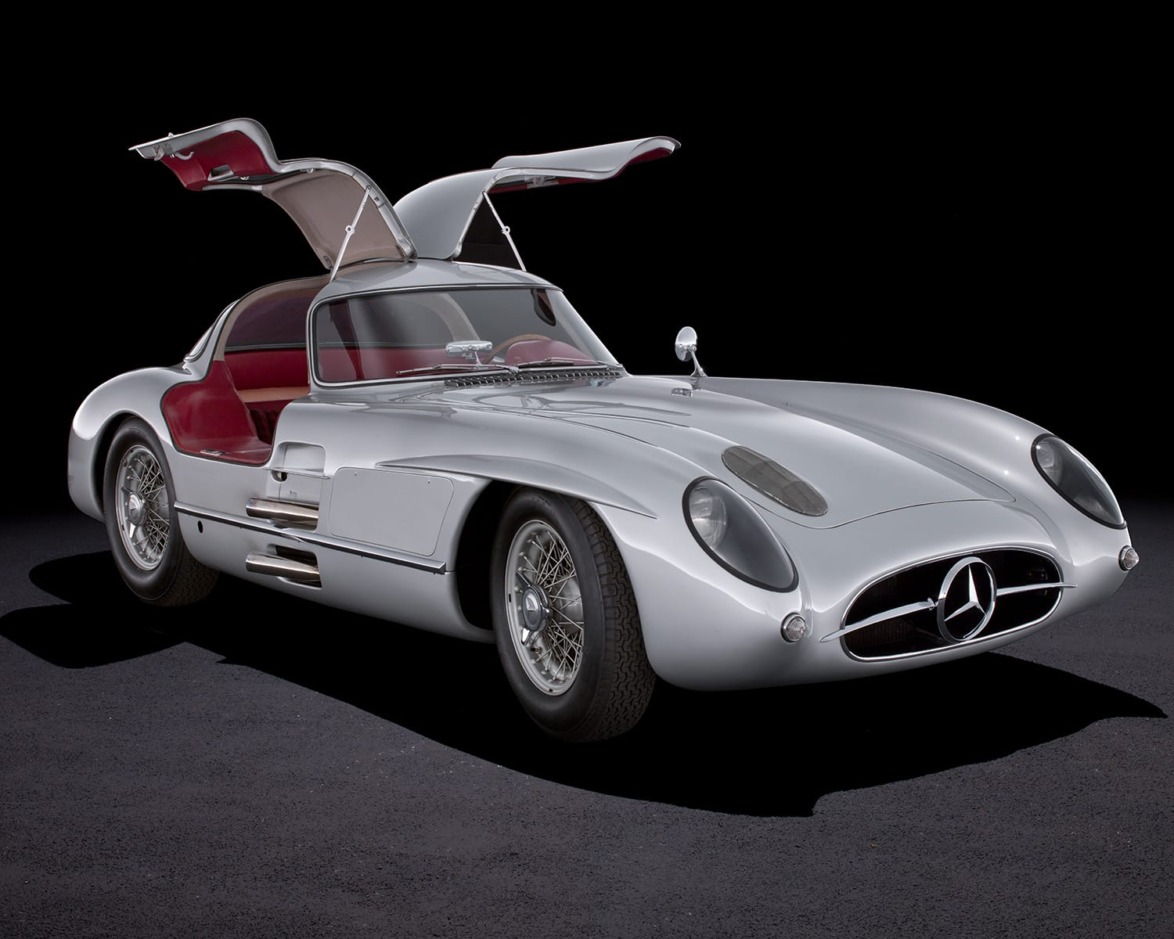 Classic silver sports car with gullwing doors open, showcasing red interior, on a dark background.