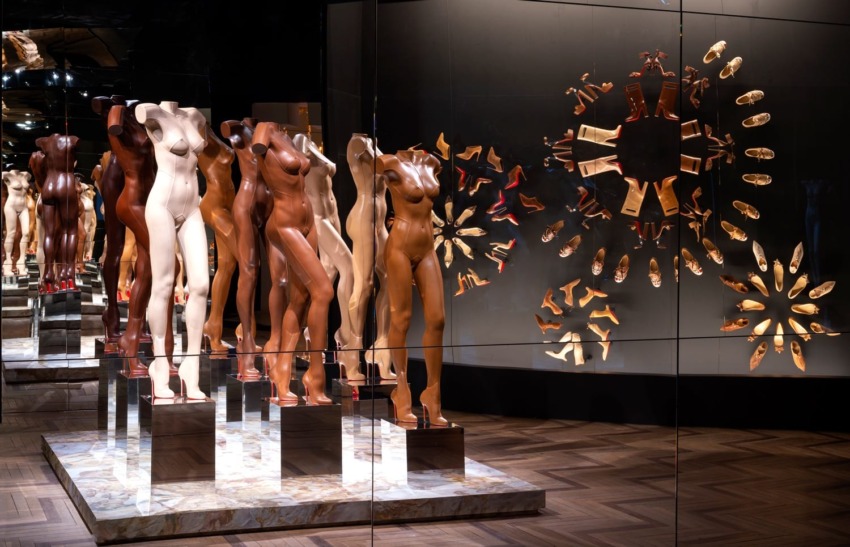 Display of mannequin torsos in varied skin tones and heels, arranged creatively with a mirrored pattern on a wooden floor.
