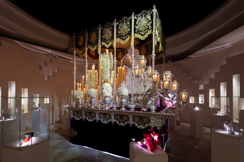 Lavishly decorated religious float adorned with candles and flowers on display in a museum setting.