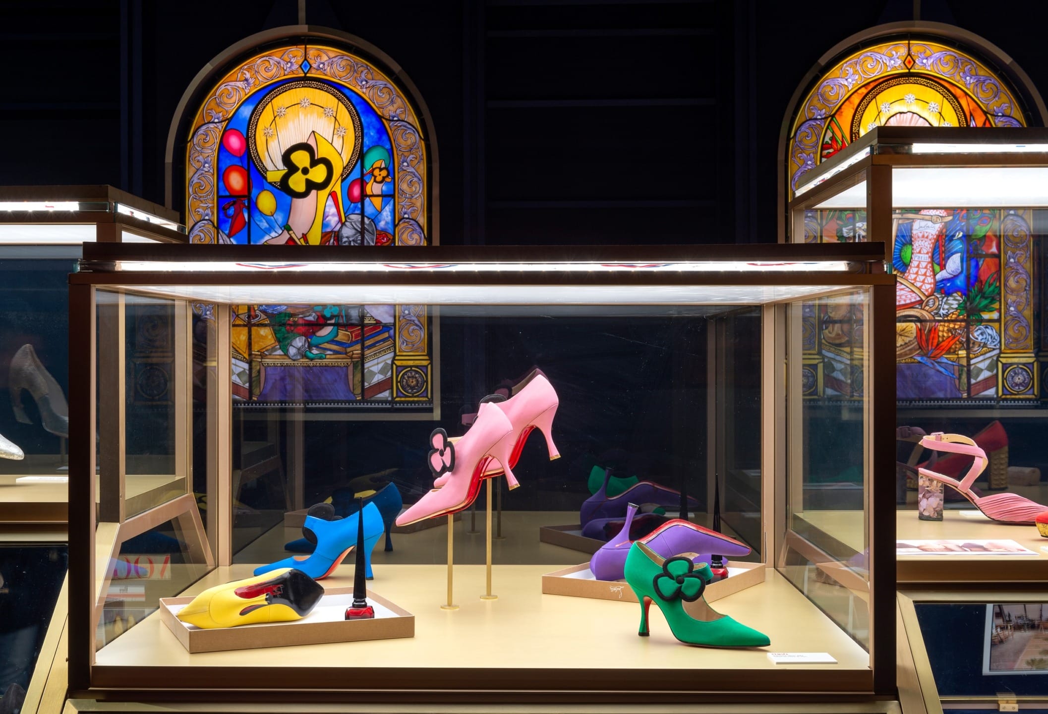 Display case with colorful high-heeled shoes and decorative stained glass background.