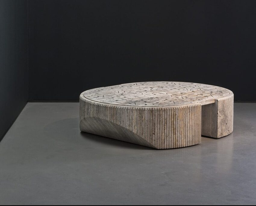 Round concrete table with intricate patterns on a smooth gray floor against a dark wall background.