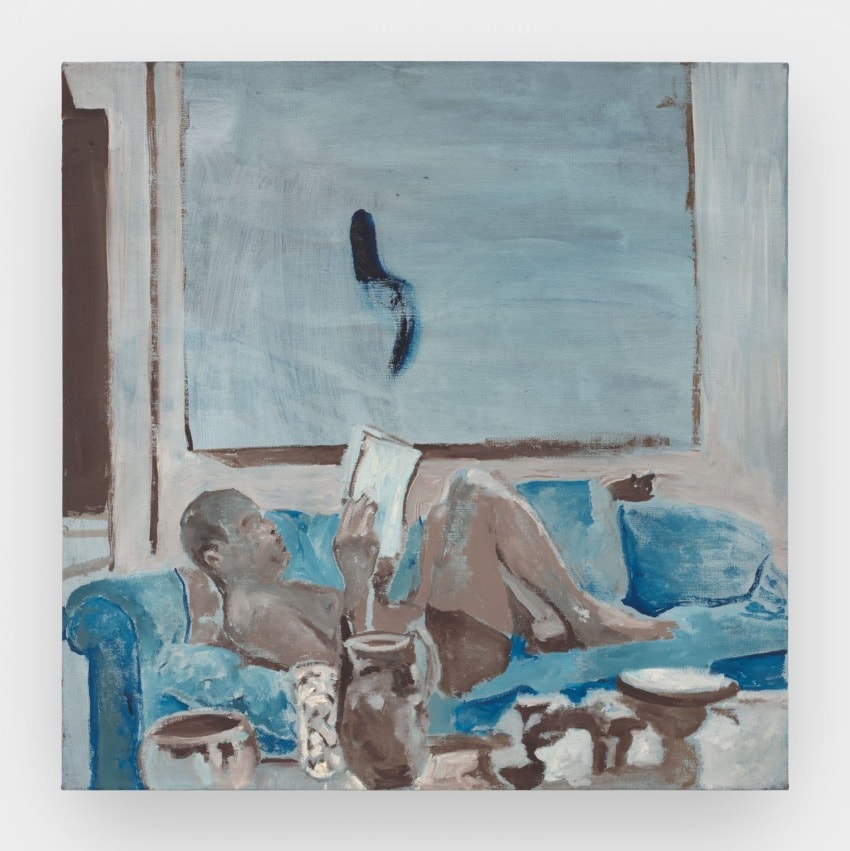Person reading on a blue sofa surrounded by various objects, with abstract artwork on the wall in muted blue tones.