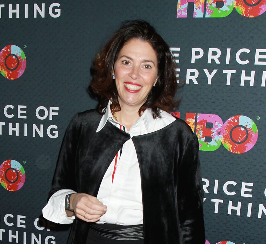 Person smiling at an event, standing in front of a background with colorful logos and text.