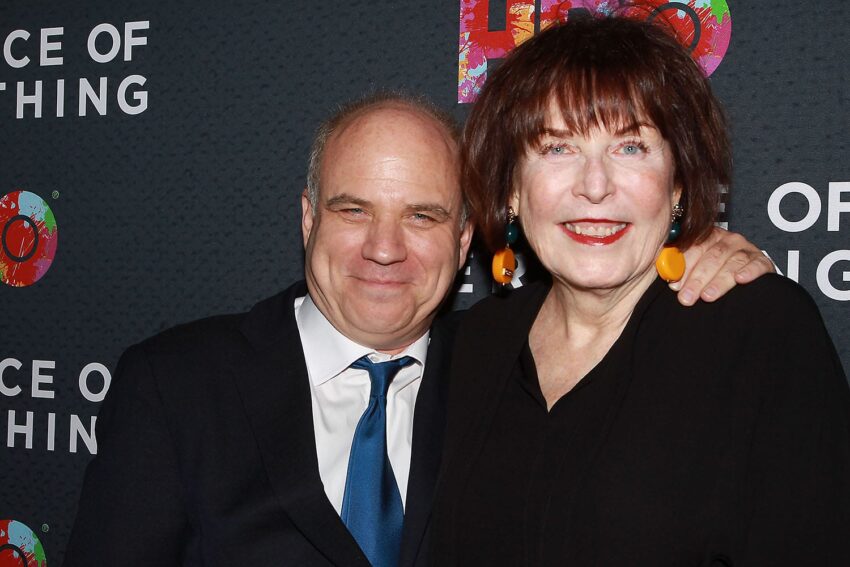 Man and woman smiling together on a red carpet event background.