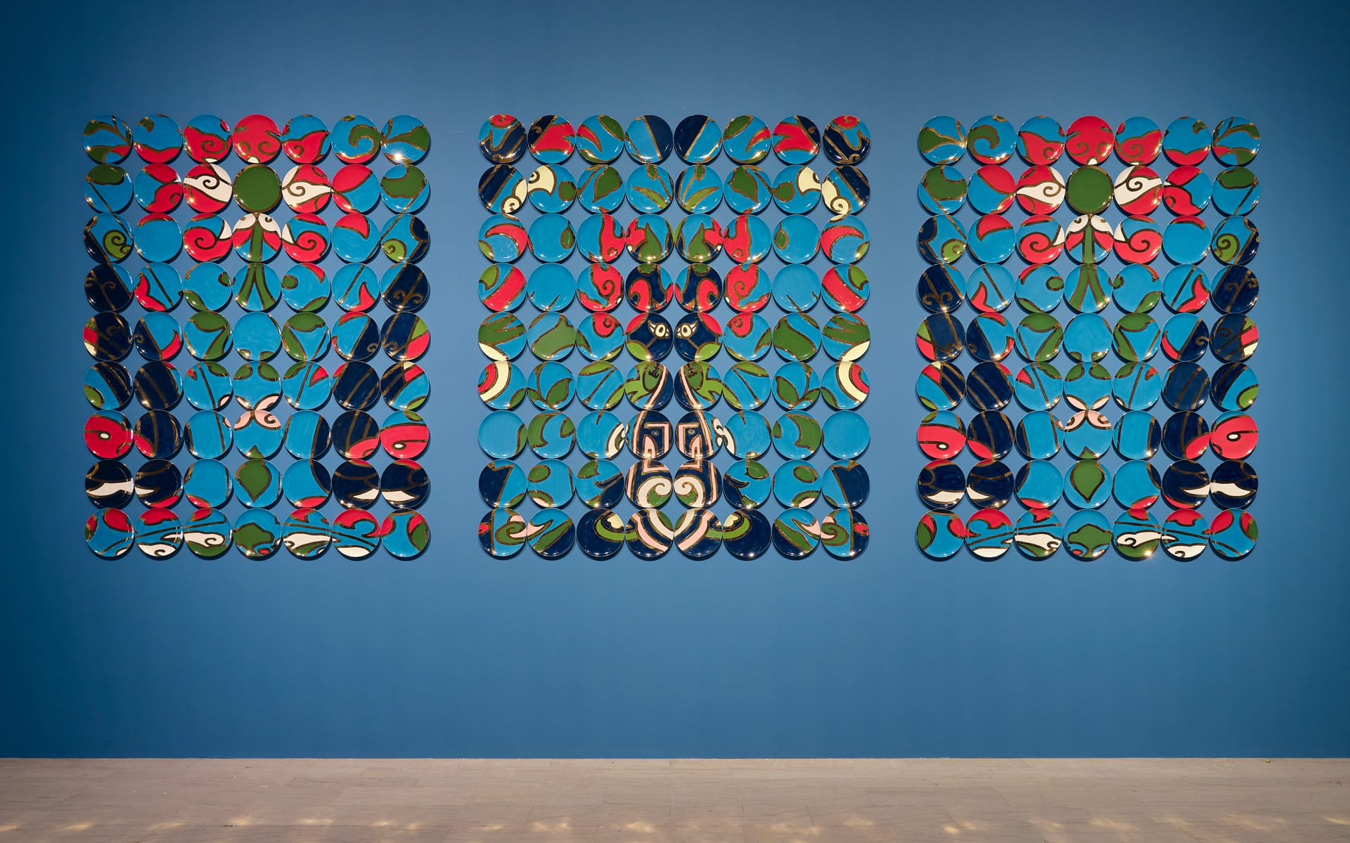 Colorful abstract art installation on blue wall, featuring symmetrical patterns with vibrant red, blue, green, and white shapes.