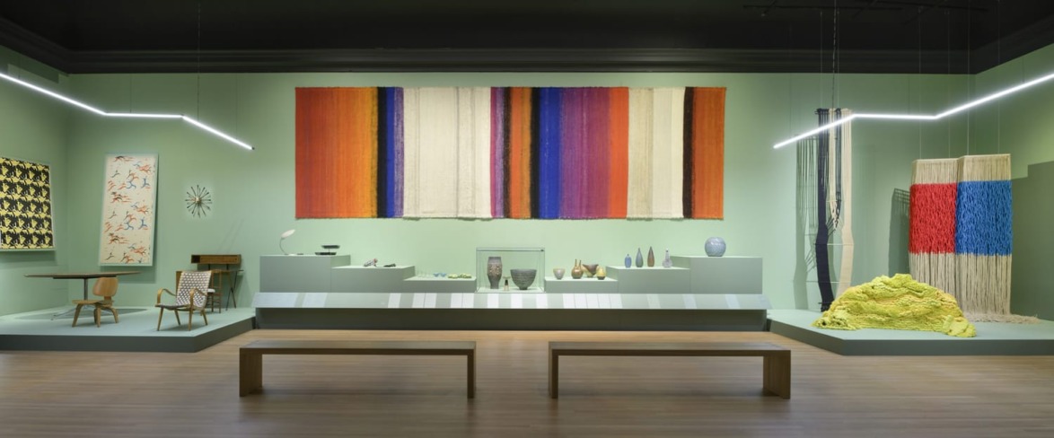 Modern art exhibit with colorful tapestries and contemporary design pieces displayed in a minimalist gallery setting.