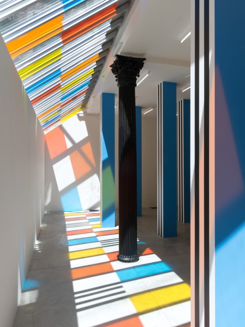 Sunlight casts colorful patterns on the floor through a modern art installation with vibrant stripes and columns.