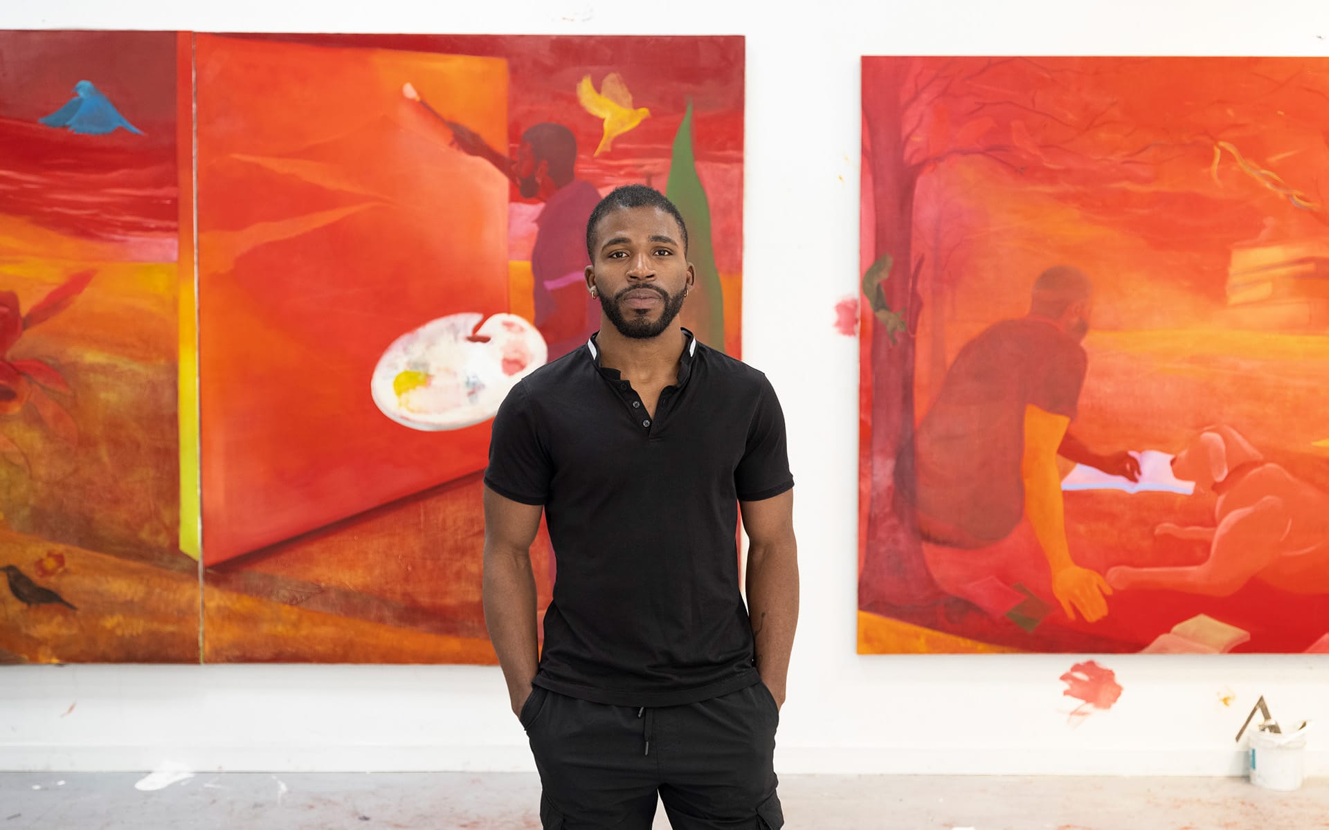 Artist standing in front of vibrant red and orange paintings in a studio setting.