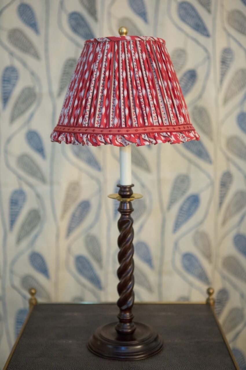 Red pleated lampshade on an ornate wooden lamp with a blue and white patterned wall in the background.