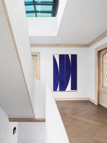 Modern interior with abstract blue painting on white wall, wooden flooring, and a skylight above.