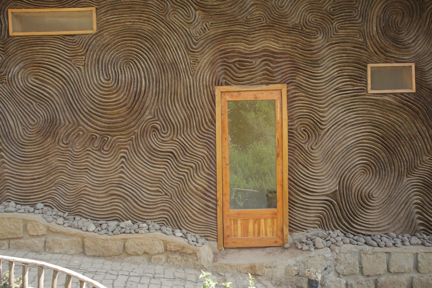 Wooden door and windows set in a wall with artistic swirling patterns.