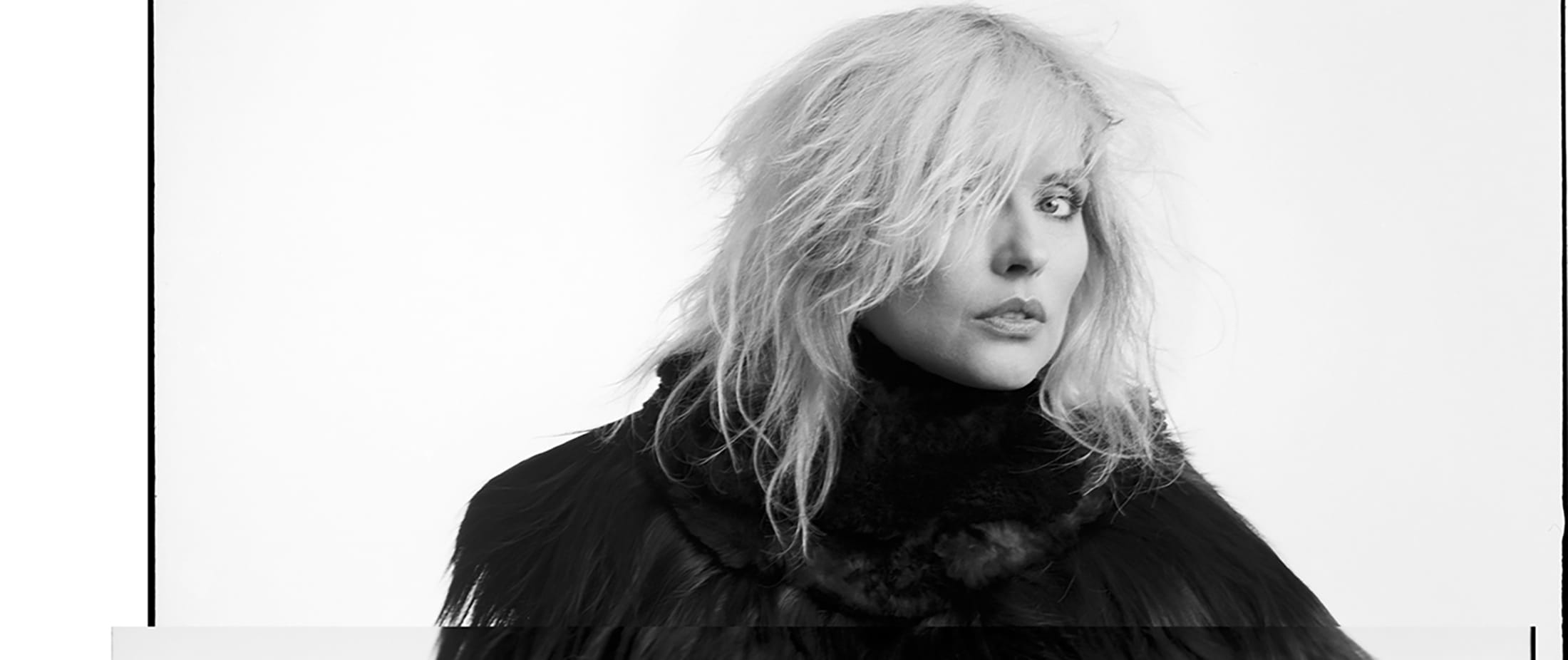 Person with light hair wearing a dark, textured outfit against a plain background.