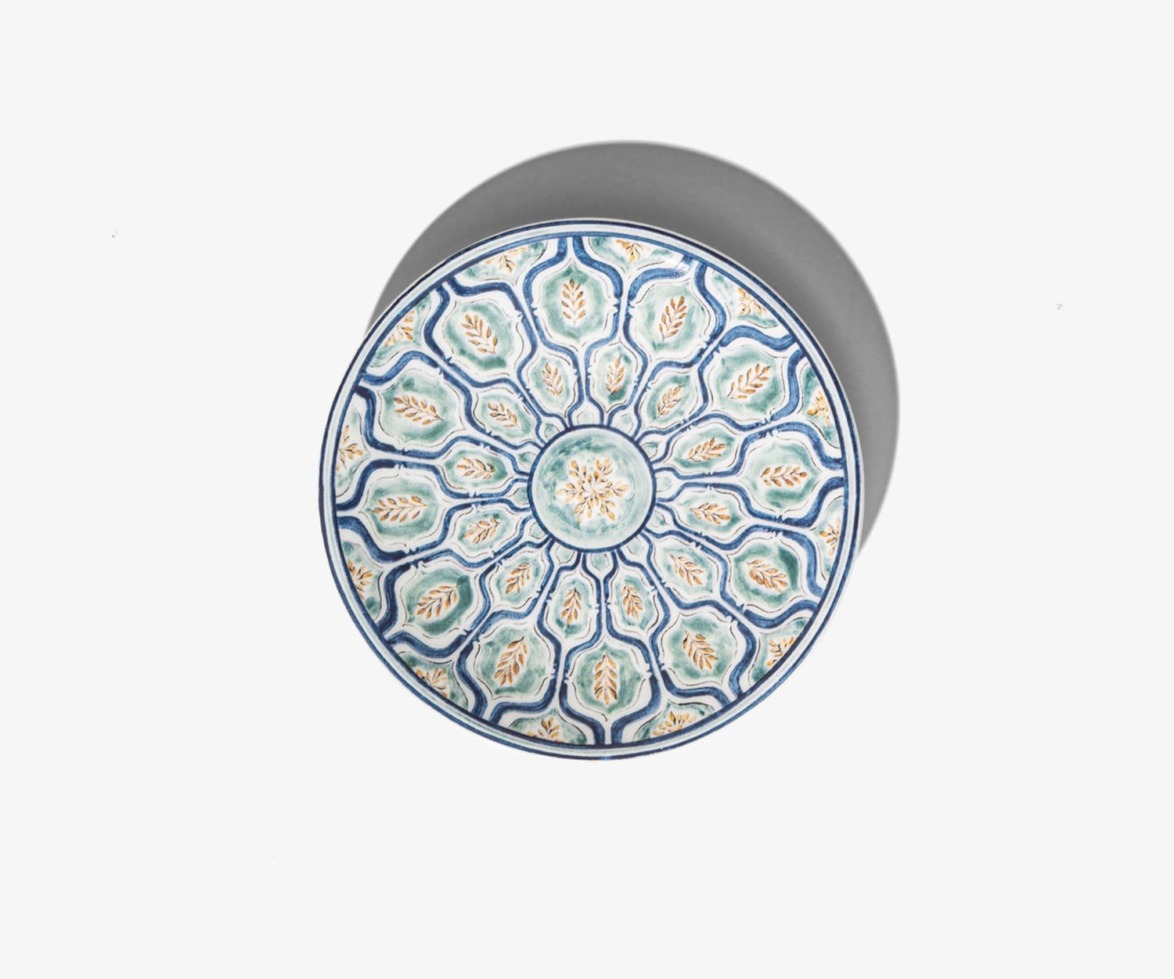 Circular ceramic plate with intricate blue and teal geometric patterns viewed from above against a plain background.