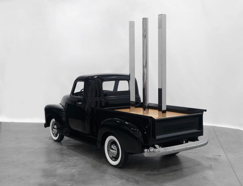 Classic black truck with a unique wooden bed and vertical metal structures in a modern garage setting.