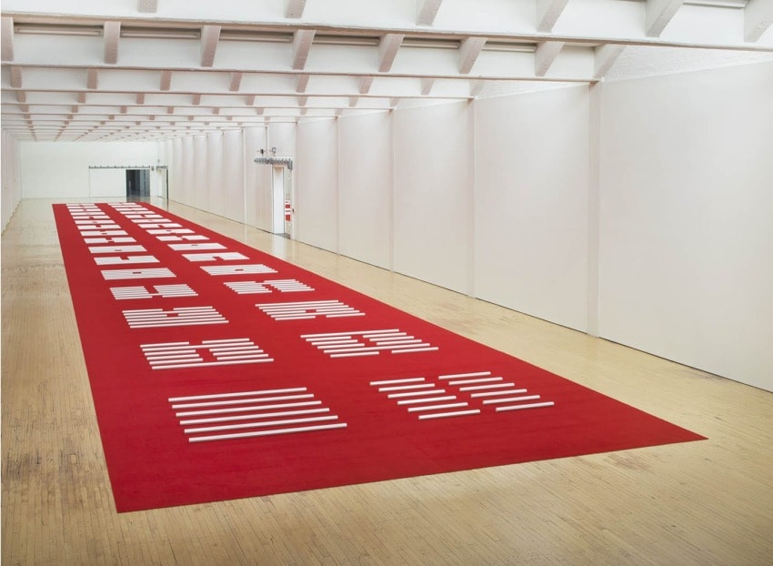 Contemporary art installation with red carpet and white geometric patterns in a spacious gallery setting.