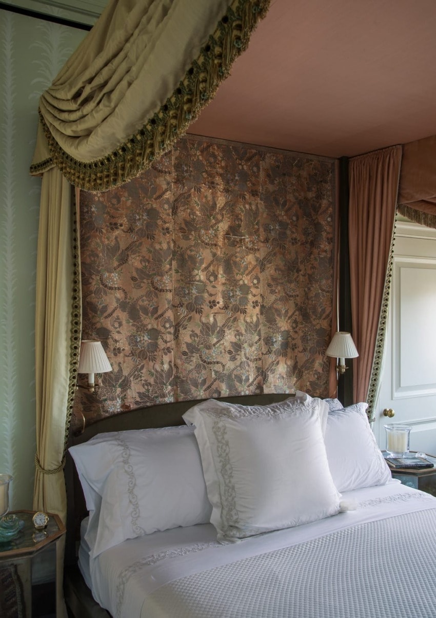 Elegant bedroom with a canopy bed, ornate headboard, white linens, and vintage bedside lamps.