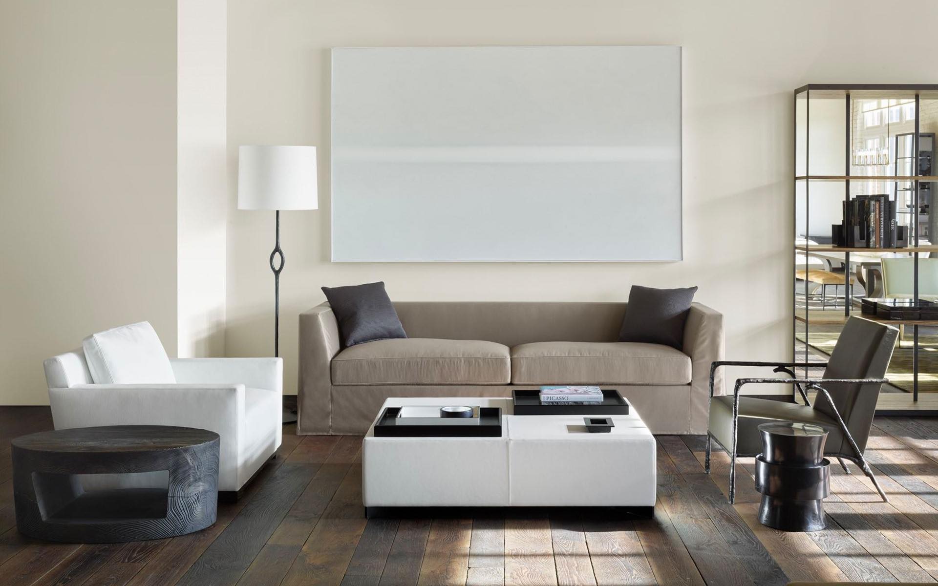 Modern living room with beige sofa, white and black chairs, floor lamp, large wall art, and mirrored cabinet.