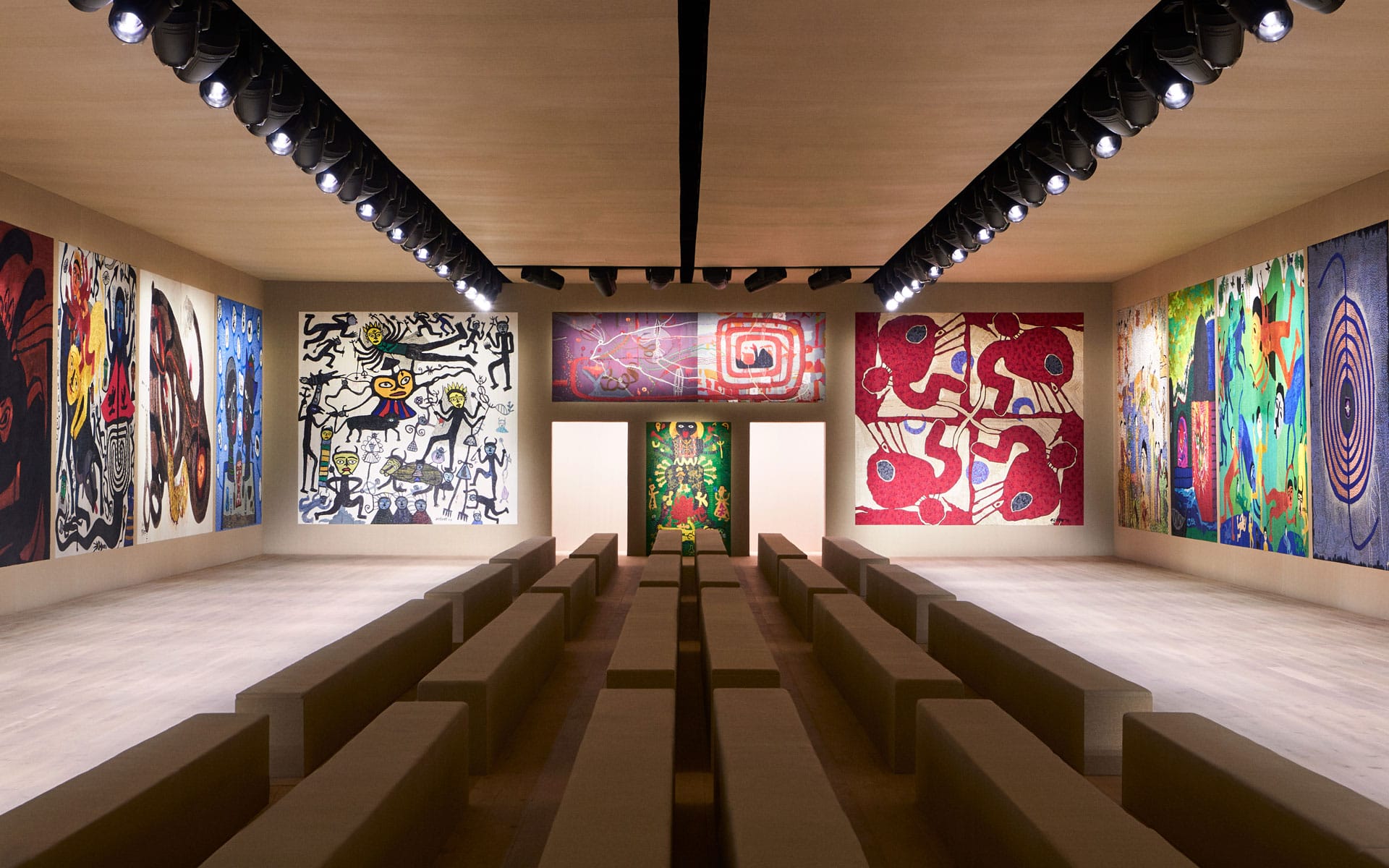 Museum exhibition space with abstract and colorful art pieces displayed on walls, illuminated by overhead spotlights.