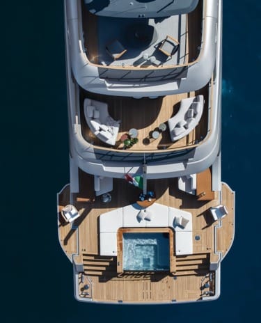 Aerial view of a luxury yacht with wooden decks, outdoor seating, and a jacuzzi on a calm ocean.