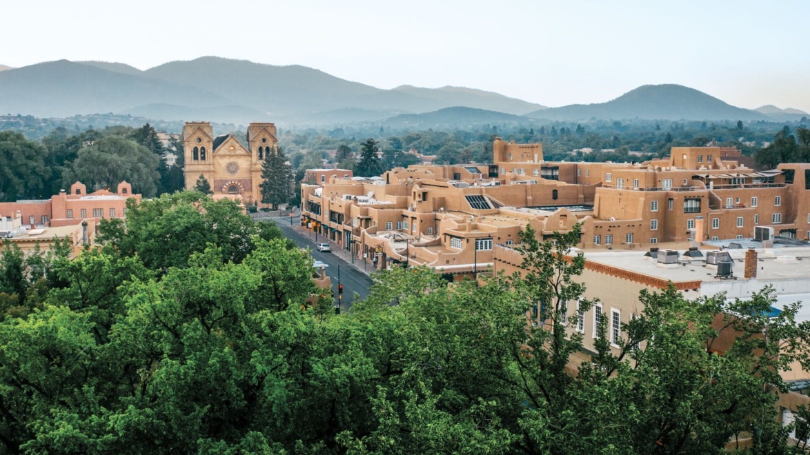 Aerial view of Santa Fe, New Mexico with adobe buildings, St. Francis Cathedral, and distant mountains.