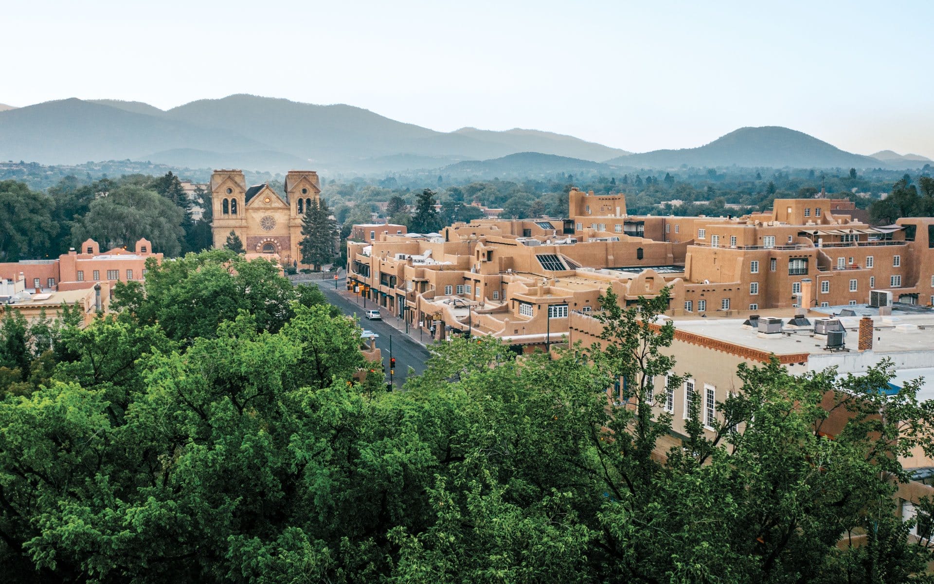 Aerial view of Santa Fe, New Mexico with adobe buildings, St. Francis Cathedral, and distant mountains.
