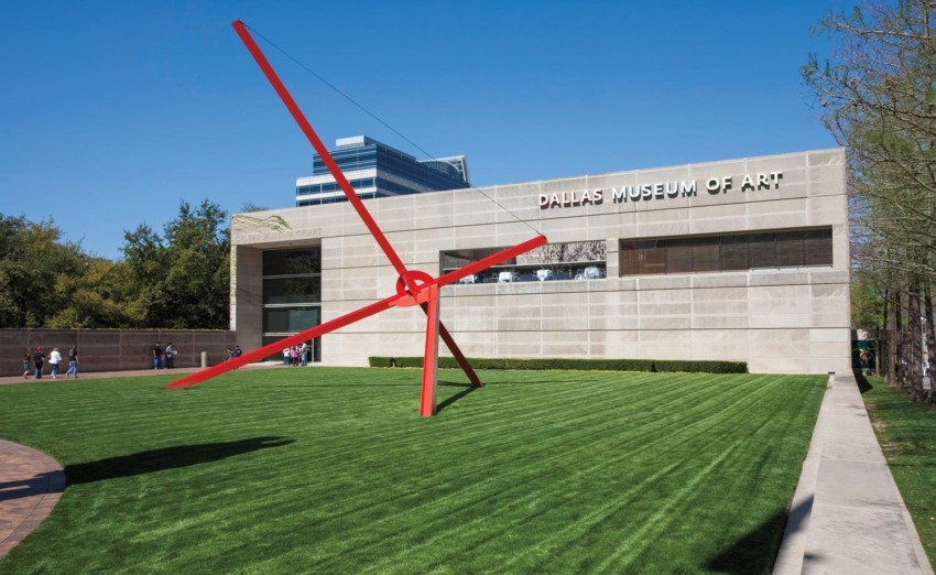 Outdoor view of Dallas Museum of Art with a large red sculpture on the grass and people walking around.