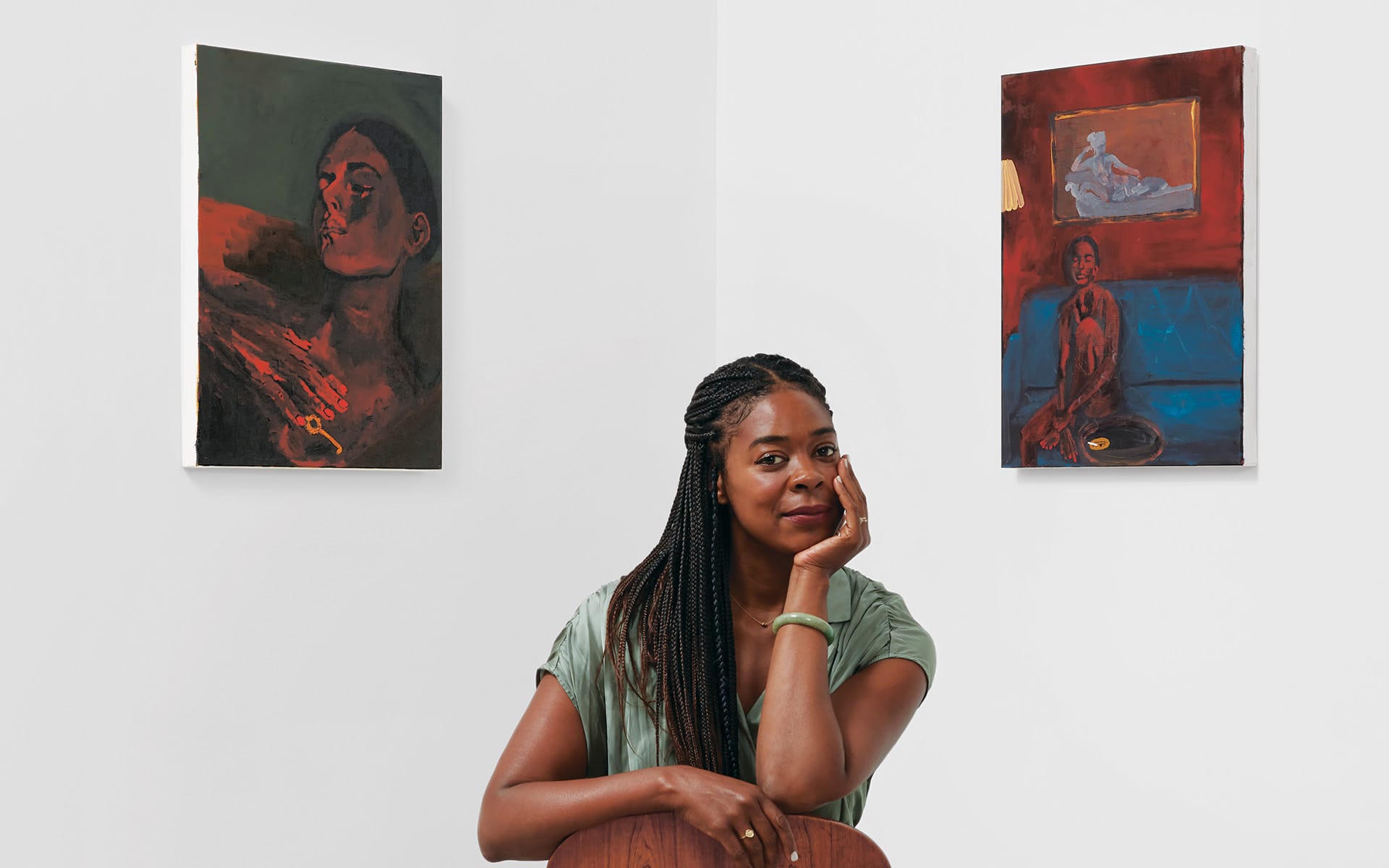 Woman sitting between two paintings in an art gallery, casually looking at the camera with a thoughtful expression.