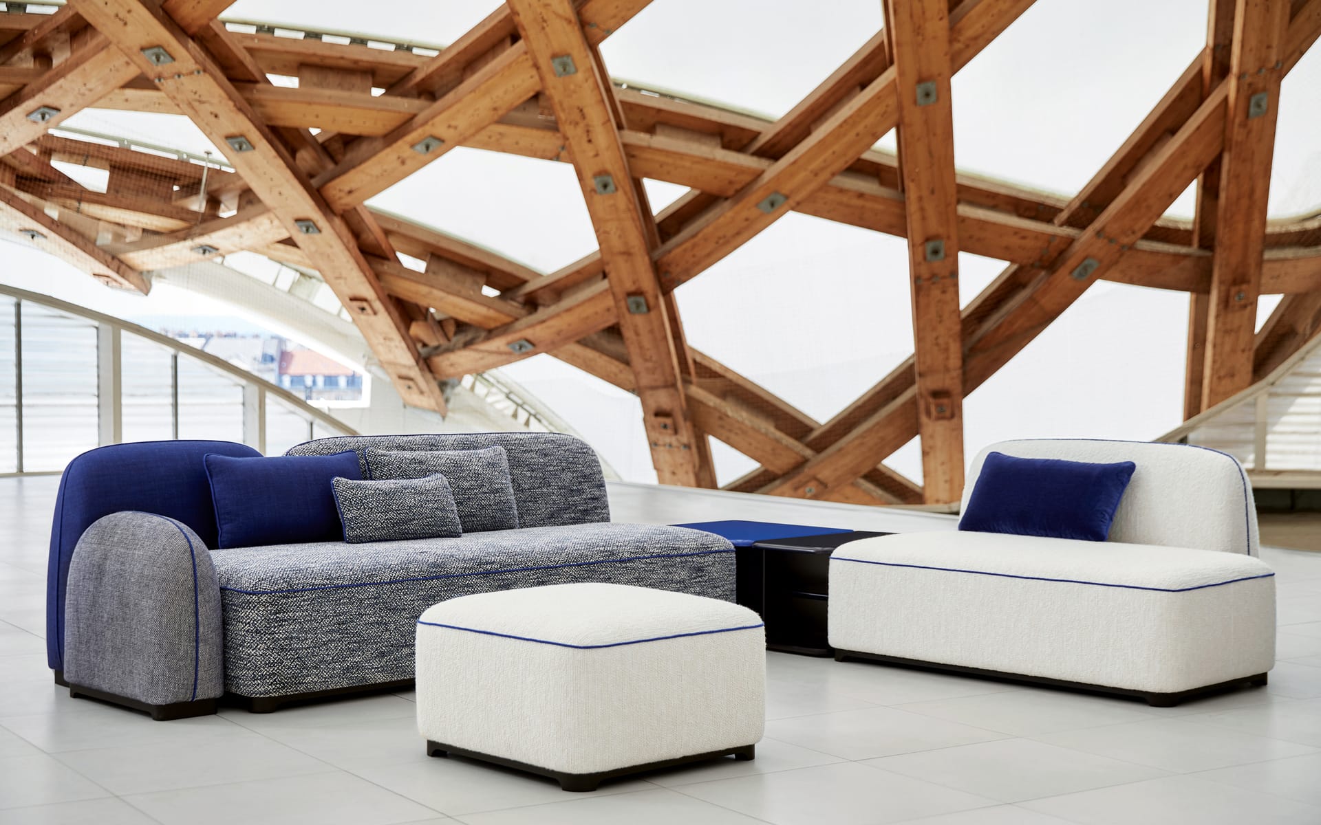 Modern furniture set with blue and white sofas and ottoman in spacious room with wooden architectural backdrop.