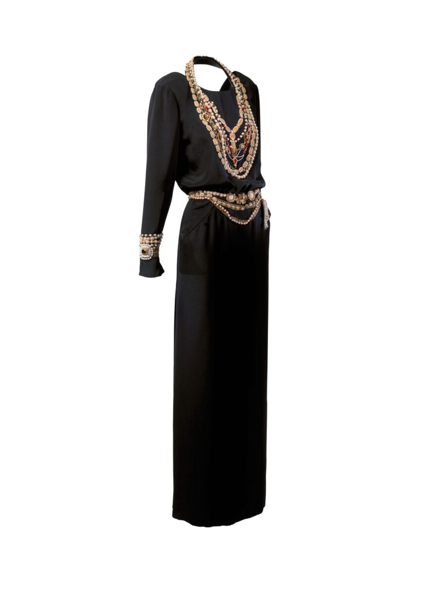 Elegant black long-sleeve dress adorned with layered gold and pearl jewelry accents on neckline, waist, and cuffs.
